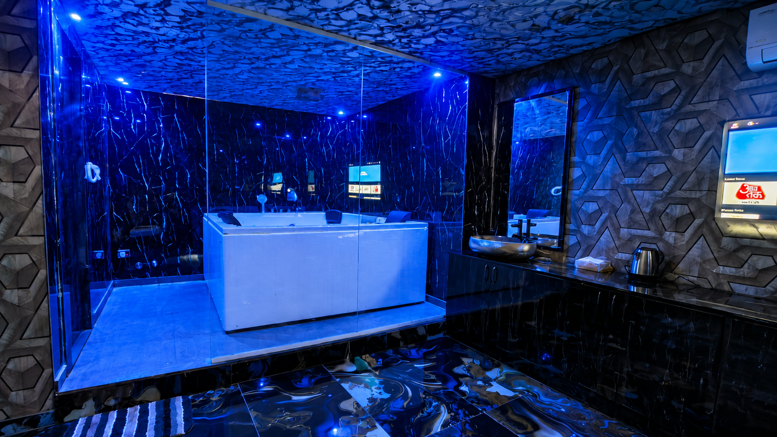 VVIP Jacuzzi suite at UNIQ International Thai Spa Marathahalli — wide-angle view with blue ambient lighting, glass-enclosed Jacuzzi, swirling marble floor, TV and vanity mirror