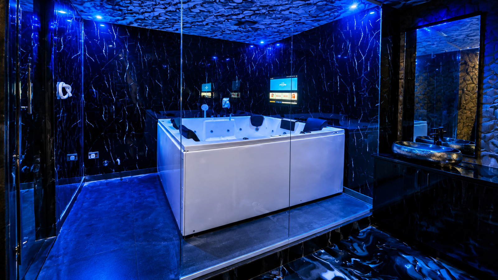 White Jacuzzi tub inside glass enclosure with blue ambient lighting and black marble walls at UNIQ International Thai Spa Marathahalli — premium private Jacuzzi retreat