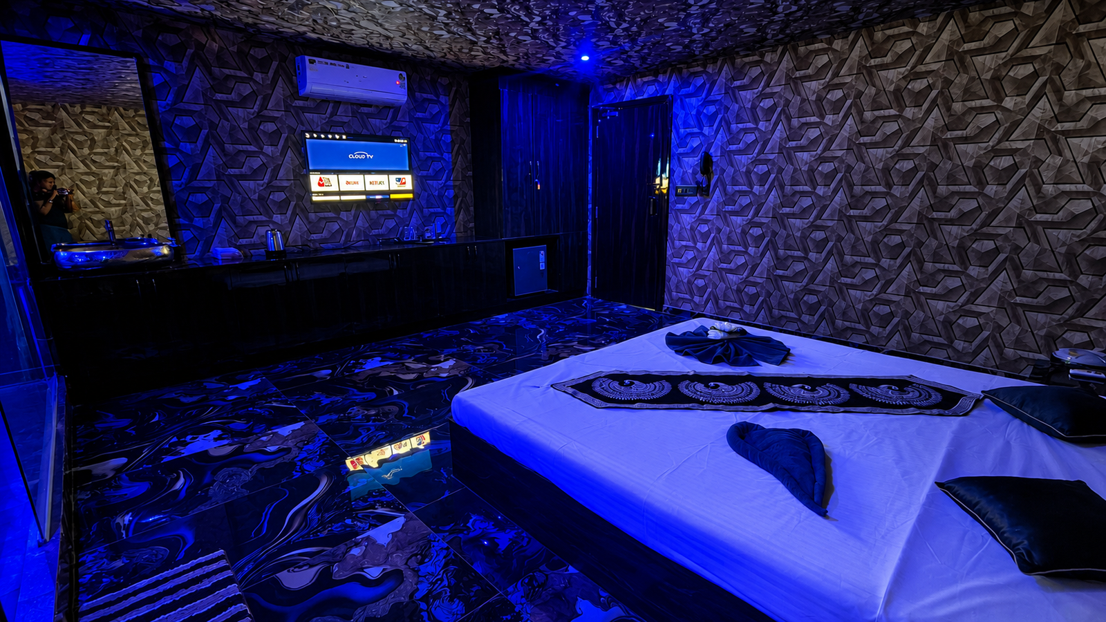 VIP private suite at UNIQ International Thai Spa Marathahalli — massage bed, blue ambient lighting, TV, black marble floors and premium spa setting