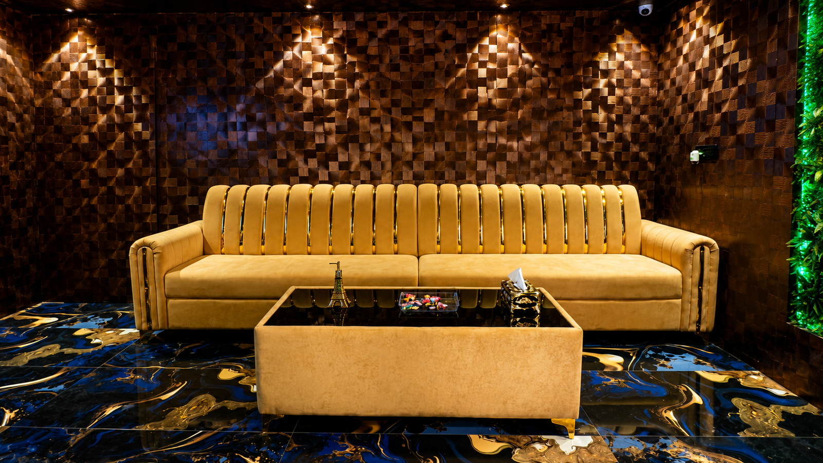 Reception waiting lounge at UNIQ International Thai Spa Marathahalli — large golden velvet sofa with gold trim, wooden textured wall, swirling marble floor and green living wall